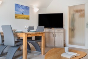 A modern dining area with a wooden table, grey chairs, and a flat-screen TV mounted on the wall. - Apartment "Bernsteinfischer" with Balcony and Wi-Fi (Zempin)