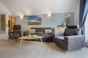 Ett modernt vardagsrum med en soffa, två fåtöljer, ett soffbord och en tavla som föreställer en strandvy.
