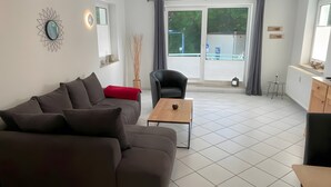 A living room with a sofa, a coffee table, a chair, and a view through a window. - Strandidyll Apartment with Balcony and Wi-Fi (Zempin)