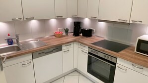 A modern kitchen with white cabinets, a stainless steel sink, a built-in oven, and a microwave. - Strandidyll Apartment with Balcony and Wi-Fi (Zempin)