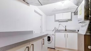 A modern kitchen with white cabinets, a built-in washing machine, and a stainless steel sink.