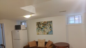 A compact living space with a sofa, a small table, a microwave on a fridge, and a window.