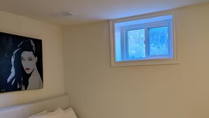 A bedroom with a single bed, a window, and a painting on the wall.