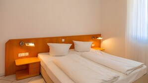 Una camera d'albergo con un letto, due comodini, una testiera e illuminazione a parete.