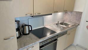 Moderni keittiö, jossa on vaaleat puukalusteet, ruostumattomasta teräksestä valmistettu pesuallas, vedenkeitin, leivänpaahdin ja astianpesukone.