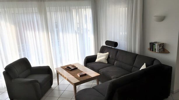 Moderni olohuone, jossa on sohva, kaksi nojatuolia, puinen sohvapöytä ja kirjahylly.