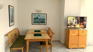 Ruokailutila, jossa on puinen pöytä ja tuolit, televisio, joka on sijoitettu kaappiin, ja seinällä on kehystettyjä kuvia.