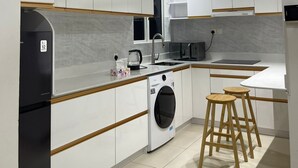 A modern kitchen with white cabinetry, a built-in washing machine, wooden stools, and a ceiling fan. - Cozy 1BR Apt in Hulhumale, Maldives - AC/WiFi (Hulhumale)