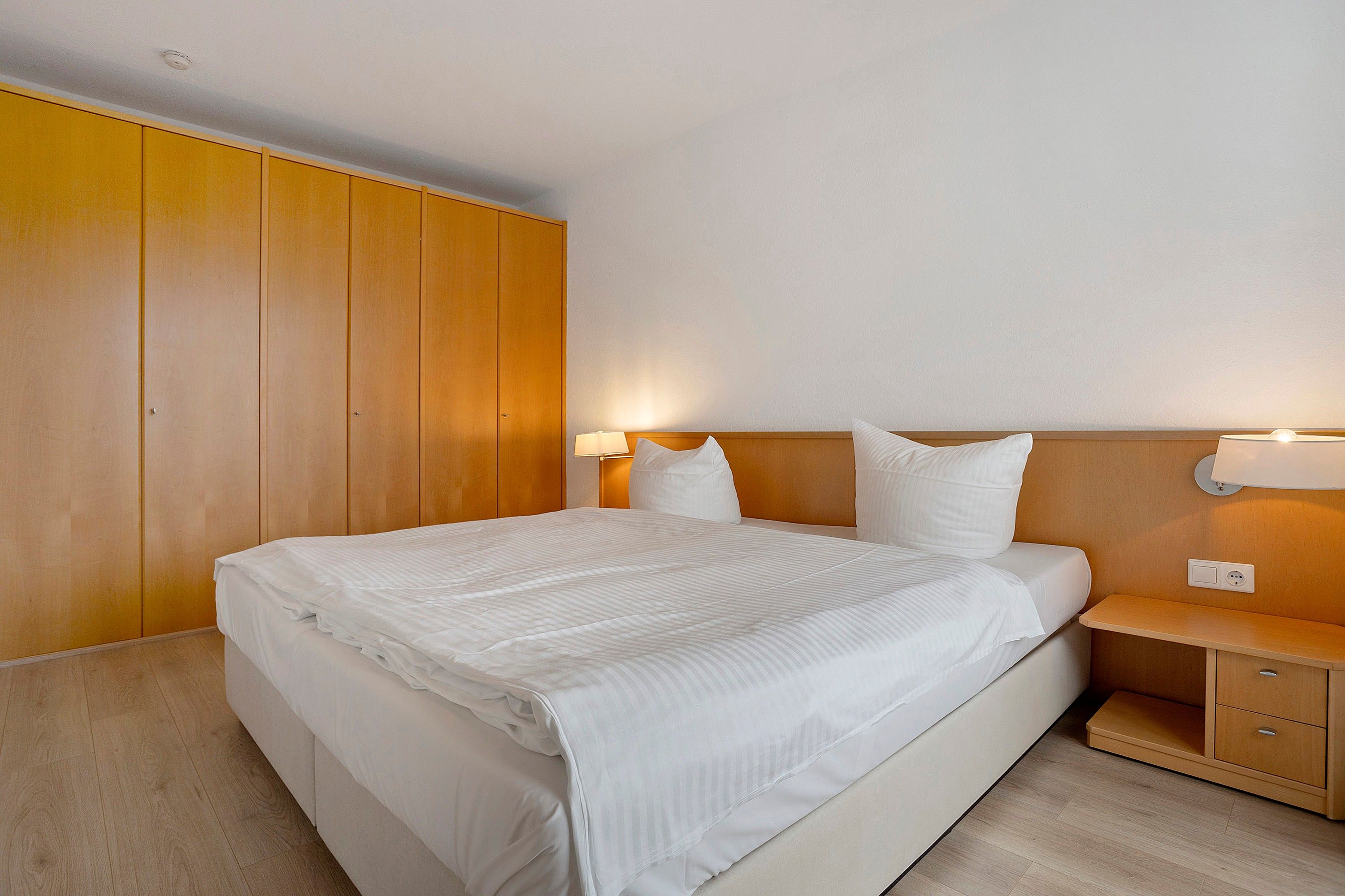 A hotel room with a large bed, wooden wardrobe, bedside tables, and a nightstand.