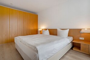 A hotel room with a large bed, wooden wardrobe, bedside tables, and a nightstand. - Apartment 'Seestern' with Balcony and Wi-Fi (Zempin)