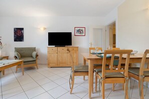 Un salon comprenant un canapé, un téléviseur, une table à manger avec des chaises et un meuble.
