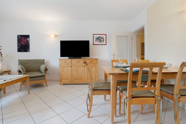 Una sala de estar con sofá, televisor, mesa de comedor con sillas y un mueble de almacenamiento.