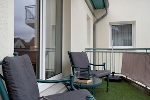 Un balcon avec deux chaises, une table en verre et une fenêtre.