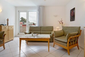 Un salon comprenant un canapé, une table en bois, une chaise, un meuble et une fenêtre avec des rideaux.