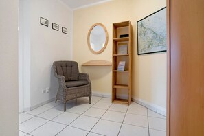 Une pièce avec un fauteuil en osier, une bibliothèque en bois, un miroir rond et une carte encadrée accrochée au mur.