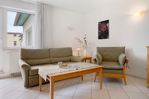 A living room with a sofa, a chair, a table, a vase with flowers, a lamp, and a framed picture on the wall. - Apartment 'Seestern' with Balcony and Wi-Fi (Zempin)
