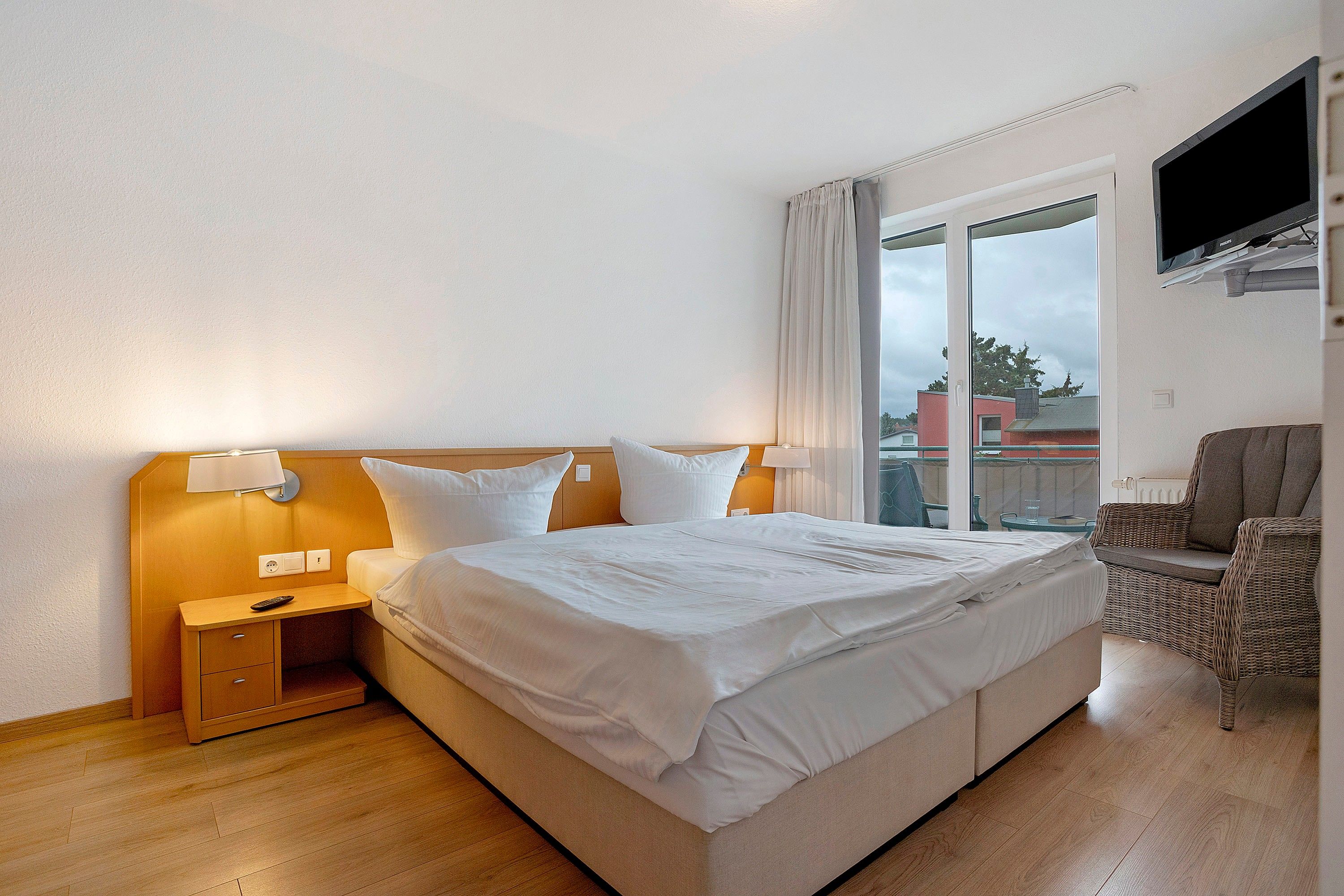 A hotel room with a bed, bedside tables, a chair, and a TV.
