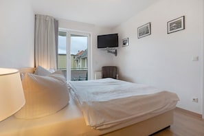 A hotel room with a bed, a chair, a TV, and a window with a view of buildings. - Apartment 'Seestern' with Balcony and Wi-Fi (Zempin)