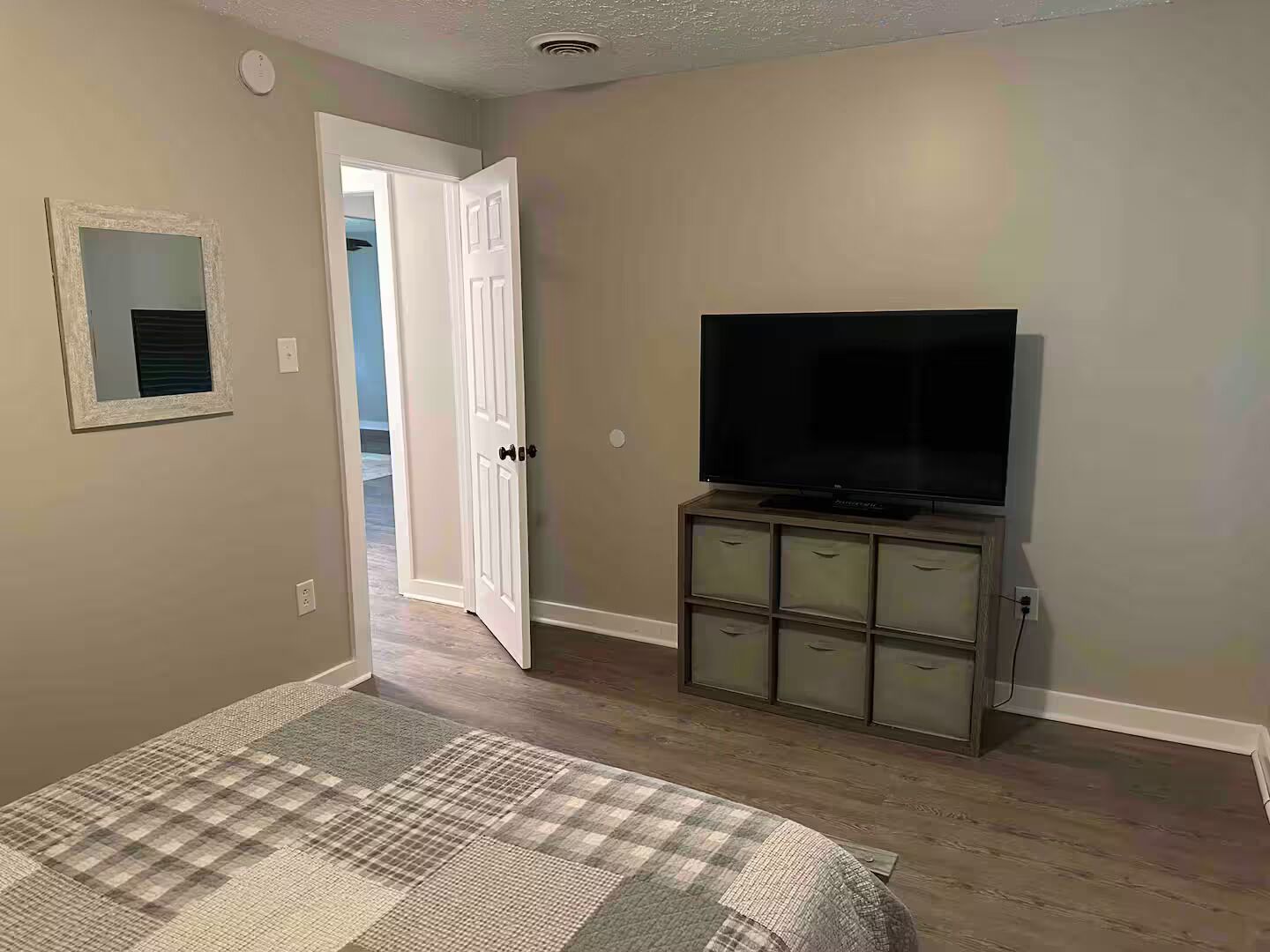 Un dormitorio con cama, televisión sobre un mueble, puerta que conduce a otra habitación y un ventanal pequeño.