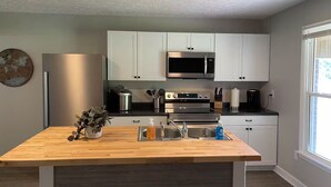 A modern kitchen with white cabinets, stainless steel appliances, and a wooden island with a sink.