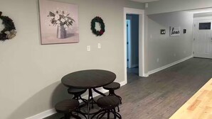 A dining area with a round table and four stools, a wall-mounted painting, and two wreaths.