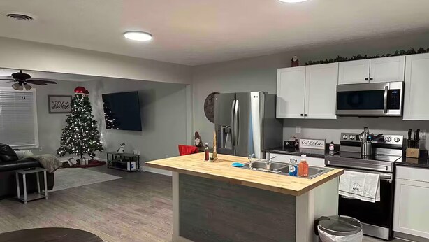 A modern kitchen with white cabinets, stainless steel appliances, a wooden island, and a Christmas tree.
