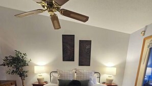 A bedroom with a bed, bedside tables, a ceiling fan, a wall-mounted artwork, and a window.