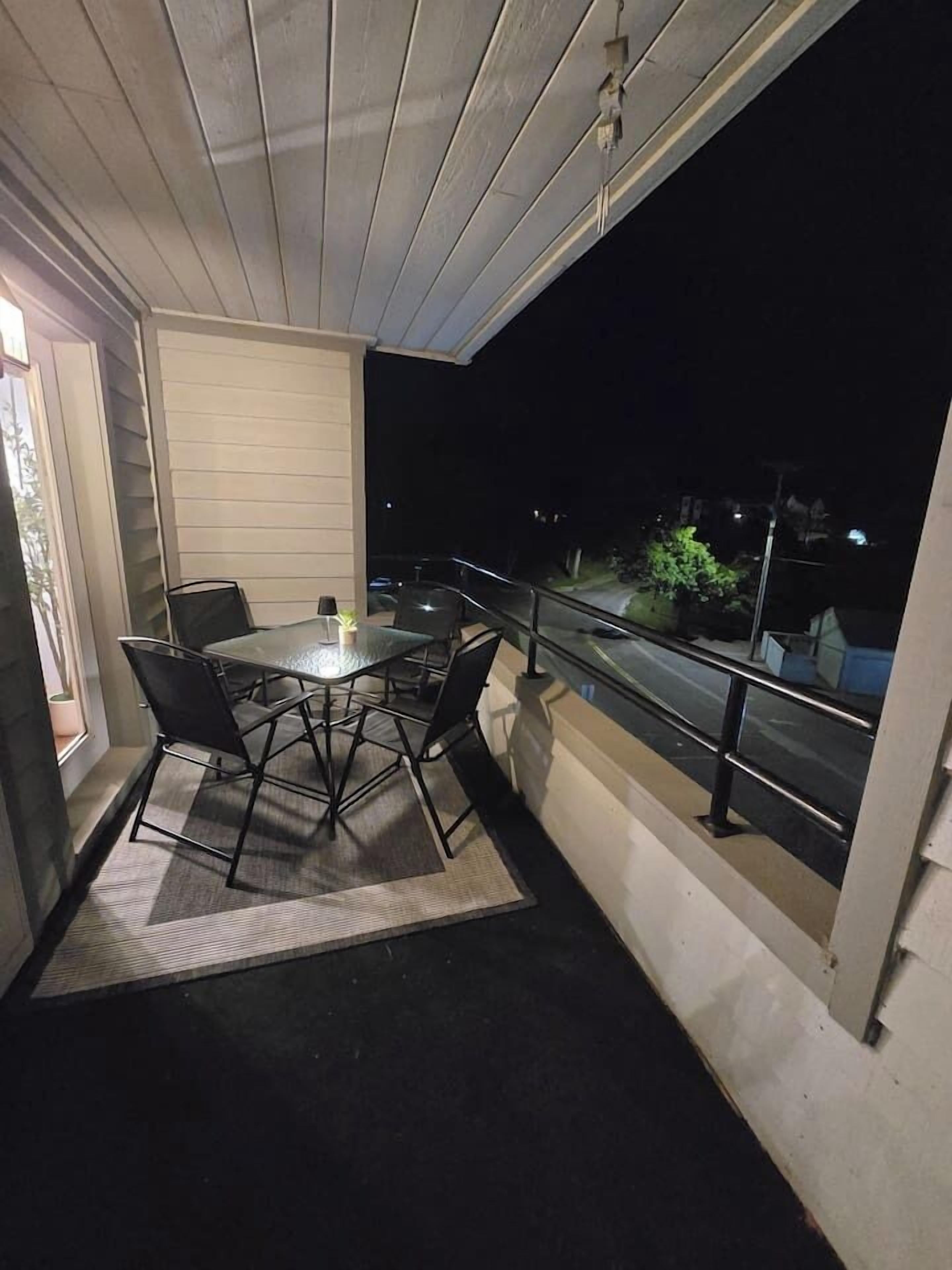 Een balkon met een tafel, stoelen, een leuning en uitzicht op de straat in de nacht.