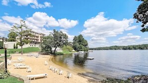 A lakeside hotel with a sandy beach, lounge chairs, and a dock.