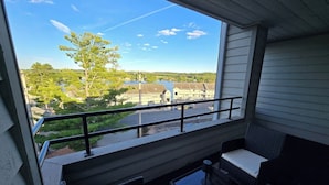 A balcony with outdoor seating, a railing, and a view of a green landscape and buildings.