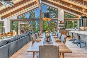Une vaste salle à manger avec une longue table en bois dressée pour le repas, entourée de sièges confortables et de grandes fenêtres offrant une vue sur l’extérieur.