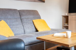A modern living room with a grey sofa, yellow cushions, a wooden coffee table, and a flat-screen TV mounted on the wall. - Apartment Ariane with Wi-Fi (Zempin)