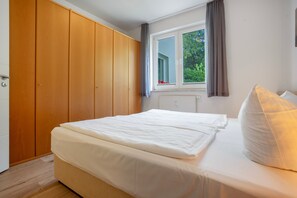 A bedroom with a bed, a wardrobe, a window with curtains, and a view of greenery outside. - Apartment Ariane with Wi-Fi (Zempin)