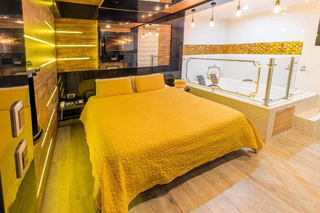 Una habitación de hotel moderna con una cama grande, un baño con cabina de vidrio y una zona de cocina.