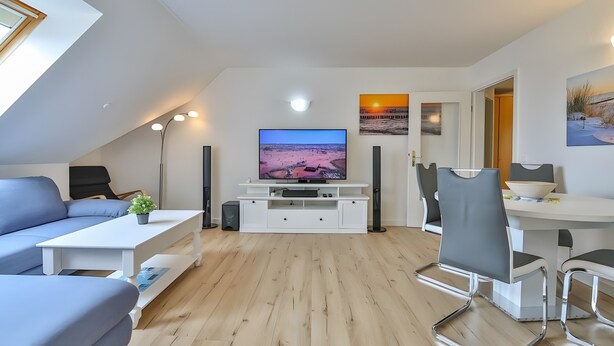 Uma sala de estar moderna com televisão de tela plana, um sofá, uma mesa de jantar e uma cozinha.