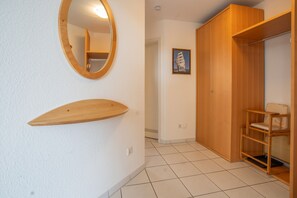 Una habitació amb un armari de fusta, una cadira de fusta petita, un mirall rodó i un quadre amb marc a la paret.