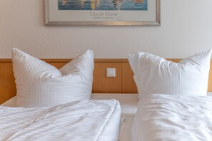 Ett hotellrum med två sängar, vita sängkläder och en inramad målning av Claude Monet på väggen.