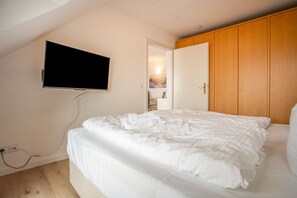 A bedroom with a bed, a television mounted on the wall, and a wooden wardrobe. - Apartment "Bella" with Balcony and Wi-Fi (Zempin)
