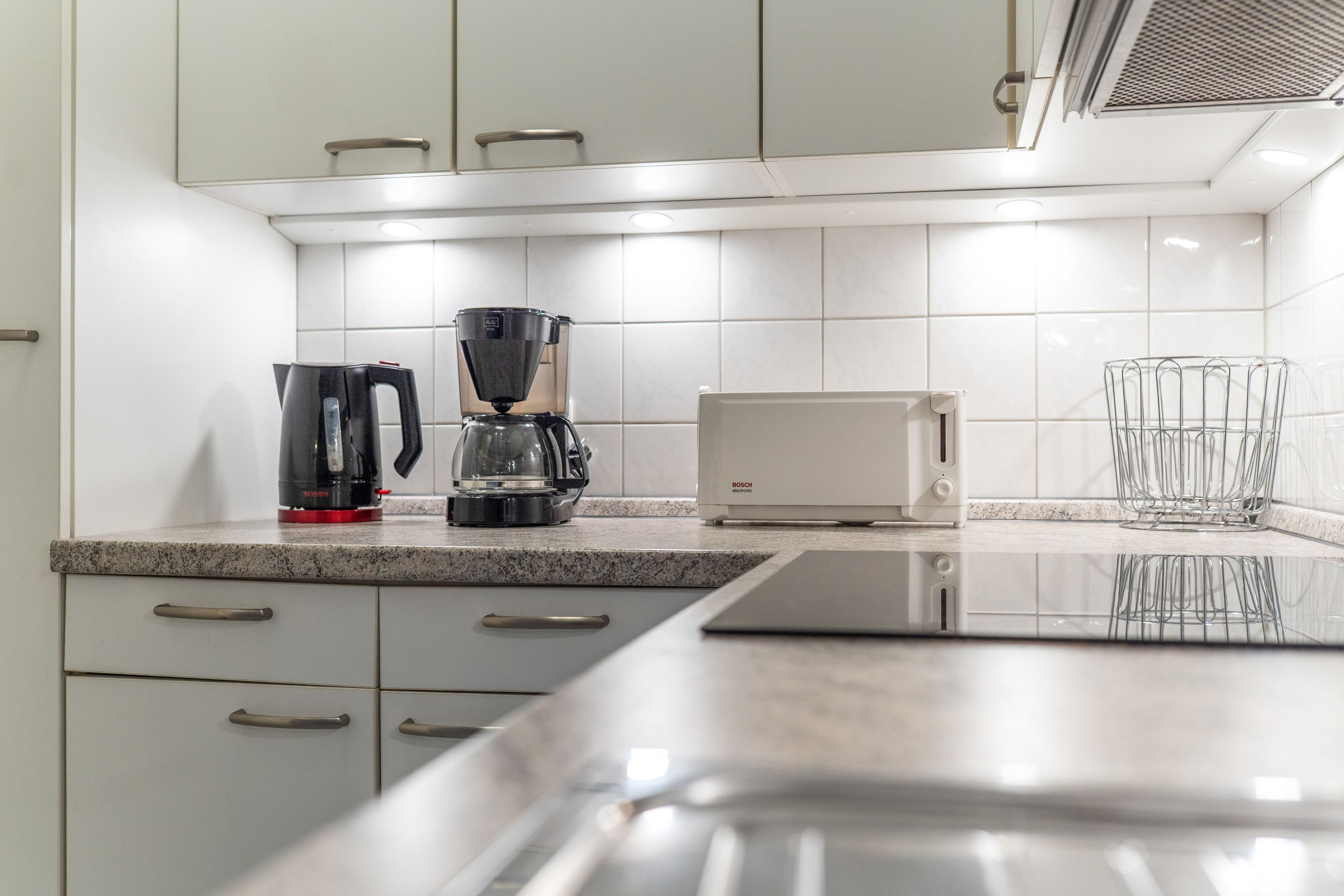 Een moderne keuken met een koffiezetapparaat, broodrooster en een glazenhouder.