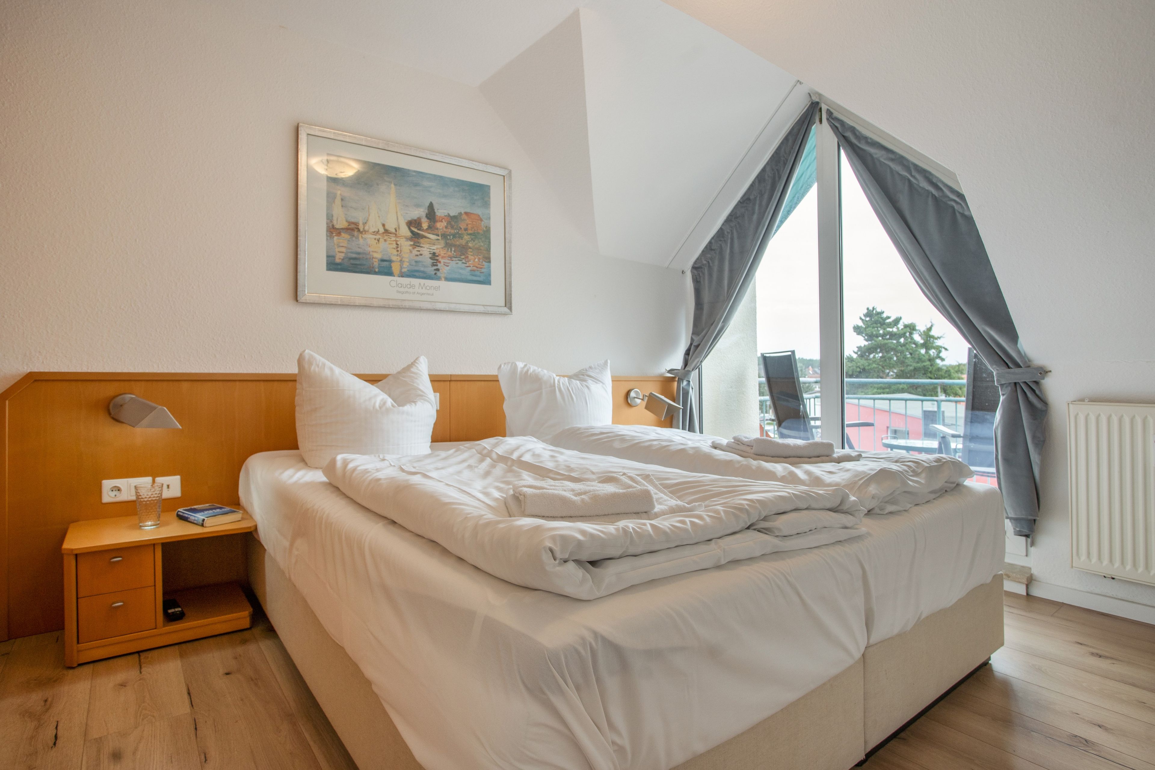 Une chambre d’hôtel avec un grand lit, une table de chevet, une commode, une fenêtre avec des rideaux et un tableau au mur.