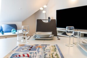 A dining table set with plates, glasses, and cutlery, with a flat-screen TV in the background. - Apartment 'Bella' with Balcony and Wi-Fi (Zempin)