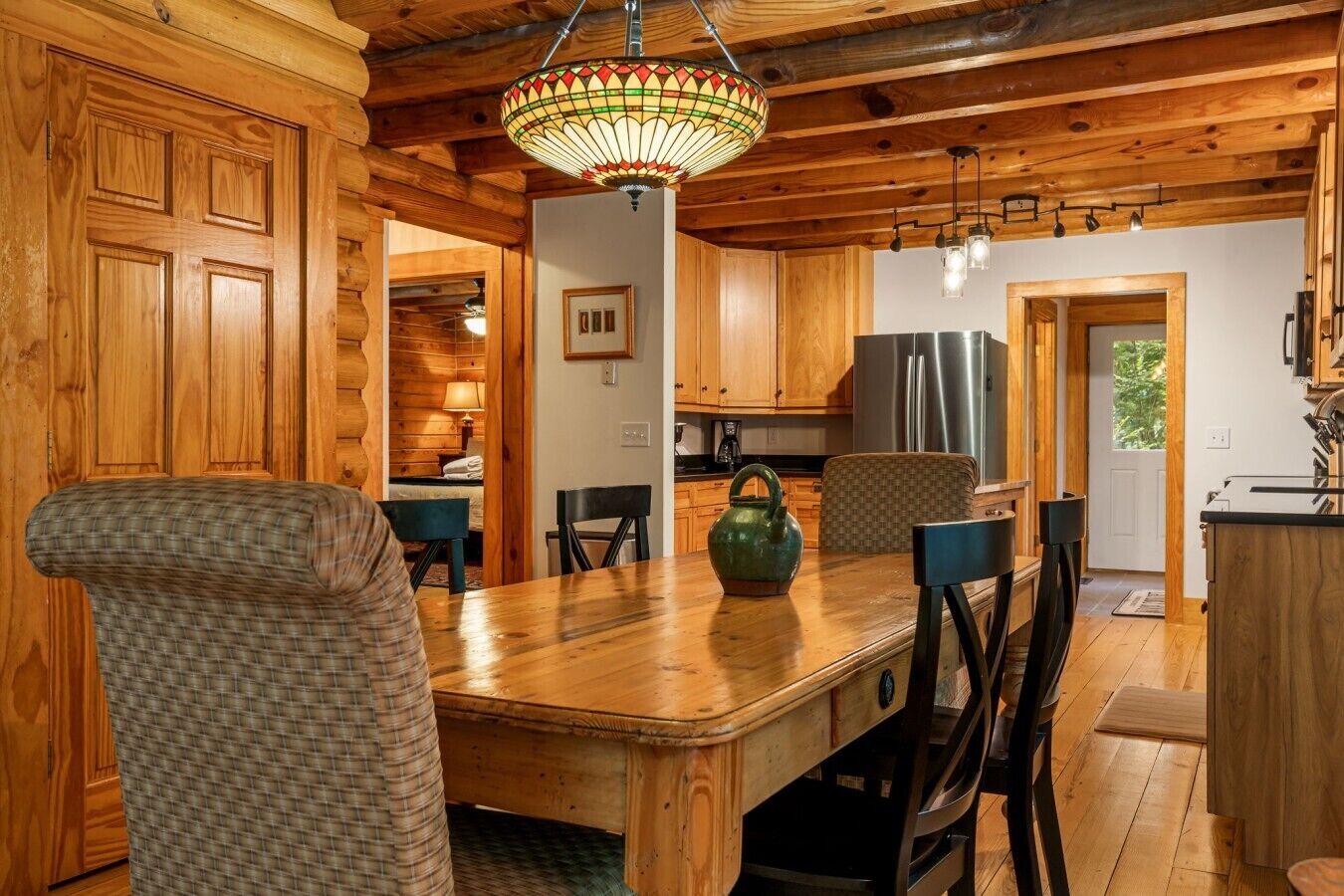 A wooden interior with a dining table, chairs, a kettle, and a refrigerator.