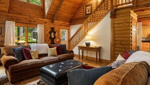 A log cabin interior with a wooden staircase, a sofa set, and a table with a lamp. - Ripple Creek Lodge | Mtn Cabin & Firepit (Cullowhee)