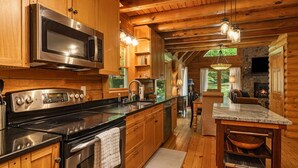 A wooden cabin interior with a kitchen, dining area, and fireplace. - Ripple Creek Lodge | Mtn Cabin & Firepit (Cullowhee)