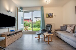A modern living room with a flat-screen TV, a wooden entertainment unit, a leather armchair, a small round table, and a sofa with decorative pillows. - Apartment 'Strandnah' with Private Terrace and Wi-Fi (Zempin)