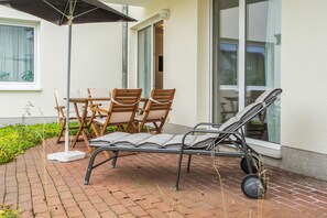 Eine Terrasse im Freien mit Tisch, Stühlen und einer Liege, beschattet durch einen großen Sonnenschirm.