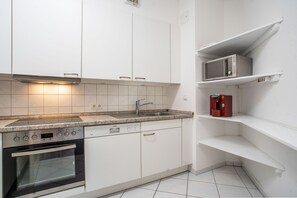 A modern kitchen with white cabinetry, a stainless steel range hood, a built-in oven, a sink with a faucet, and a microwave on a white shelf. - Apartment 'Strandnah' with Private Terrace and Wi-Fi (Zempin)