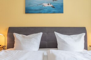 Ein Bett mit weißen Leinen und zwei Kissen, ein dunkles Kopfteil sowie ein Gemälde von Vögeln, die über Wasser fliegen, an der Wand.