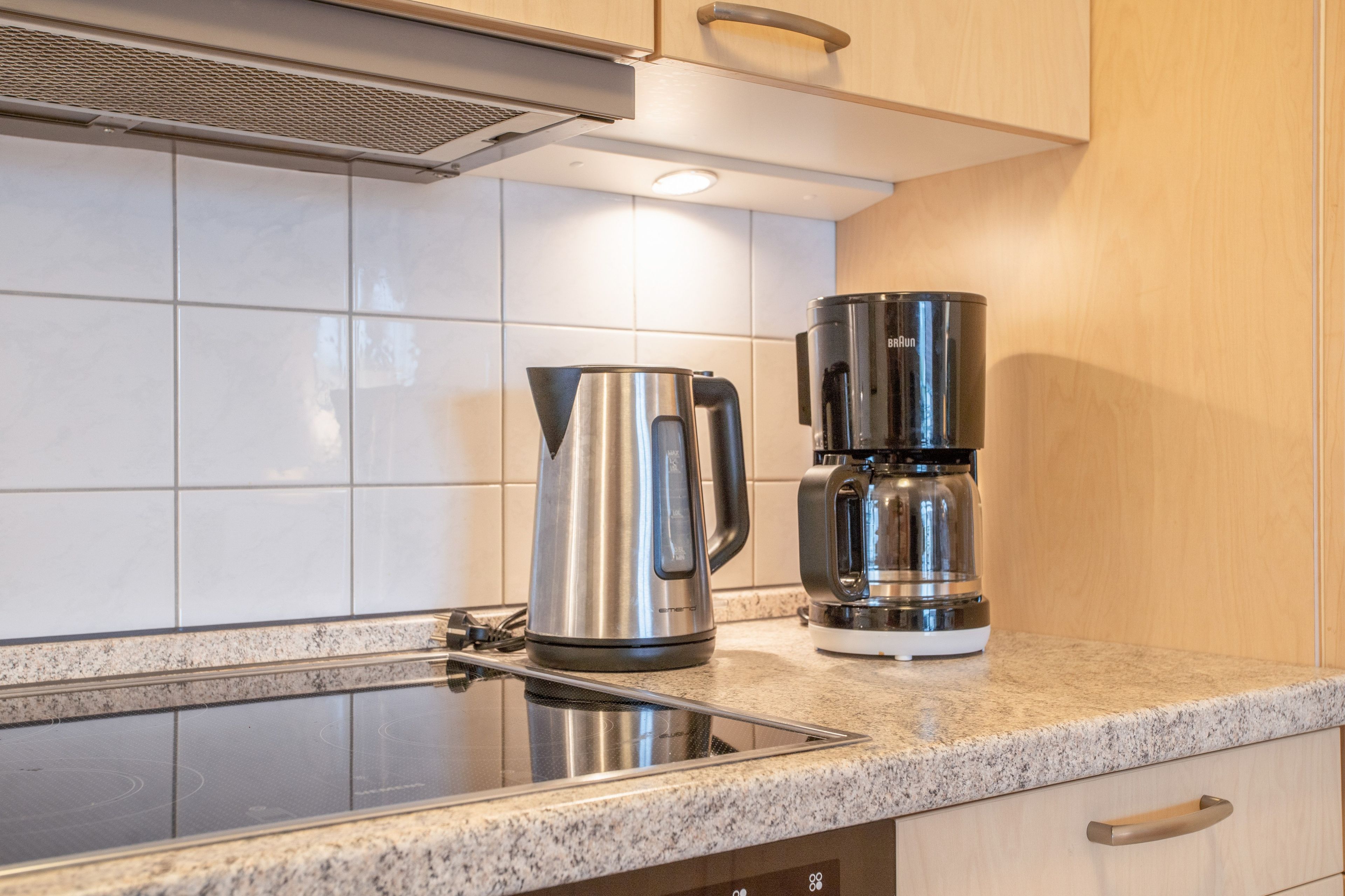 A kitchen with a stainless steel kettle and a coffee maker on the countertop.