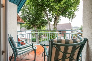 Een balkon met twee stoelen en een kleine tafel, met uitzicht op een straat met gebouwen en bomen.